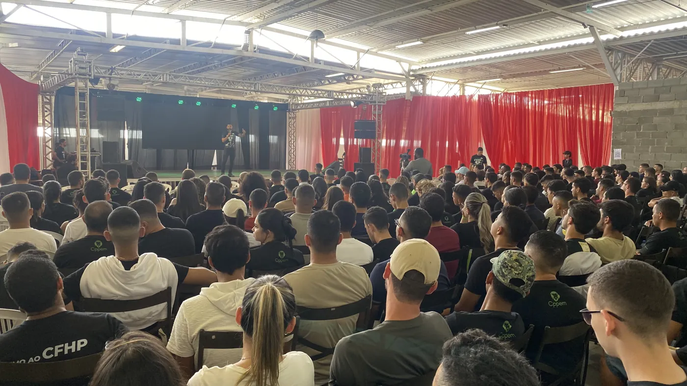 Professor no palco falando para o auditório cheio, visto do fundo da plateia